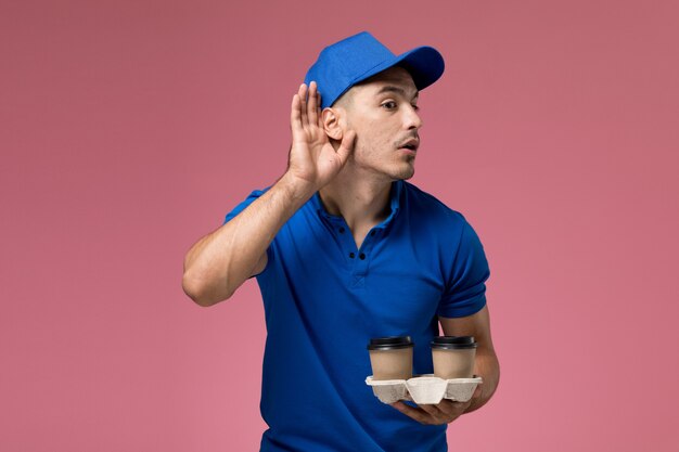 mannelijke koerier in blauw uniform met koffiekopjes proberen te horen op roze, uniforme dienstverlening