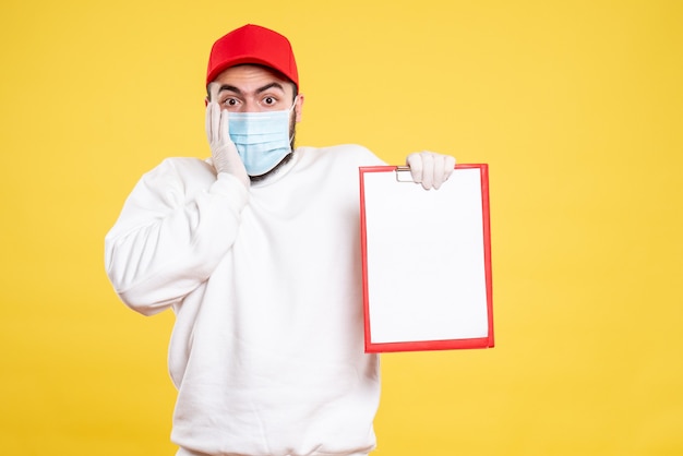 Gratis foto mannelijke koerier in masker met bestandsnotitie op geel