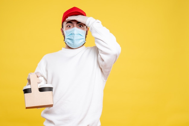 mannelijke koerier in masker met bezorgkoffie op geel