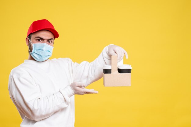 Mannelijke koerier in masker met bezorgkoffie op geel