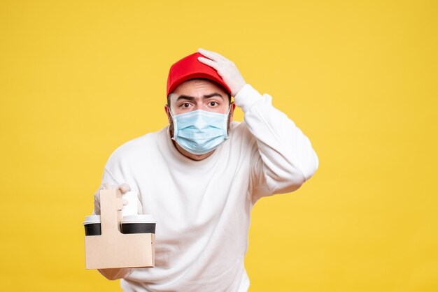 mannelijke koerier in masker met bezorgkoffie op geel