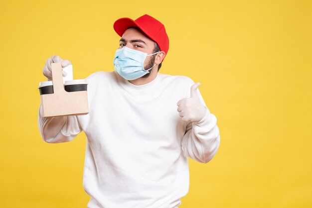 mannelijke koerier in masker met bezorgkoffie op geel