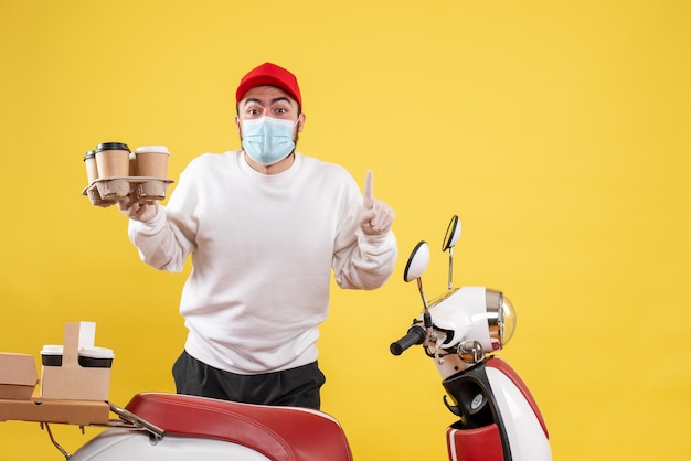 mannelijke koerier in masker met koffie op geel holding