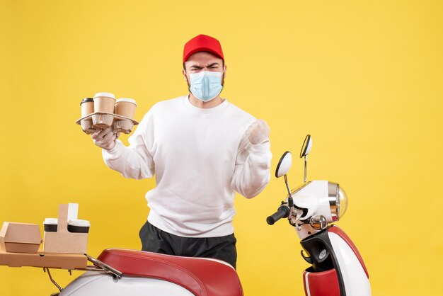 mannelijke koerier in masker met koffie op geel holding