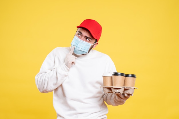 mannelijke koerier in masker met koffie op geel holding