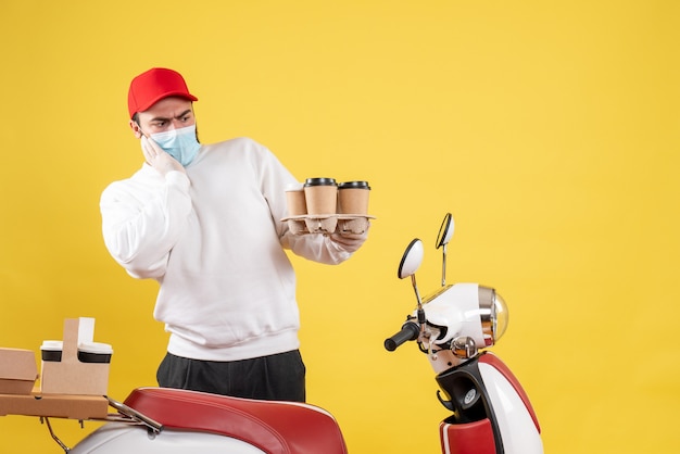 mannelijke koerier in masker met koffie op geel holding