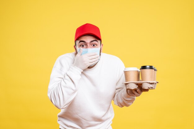 mannelijke koerier in masker met koffie op geel holding