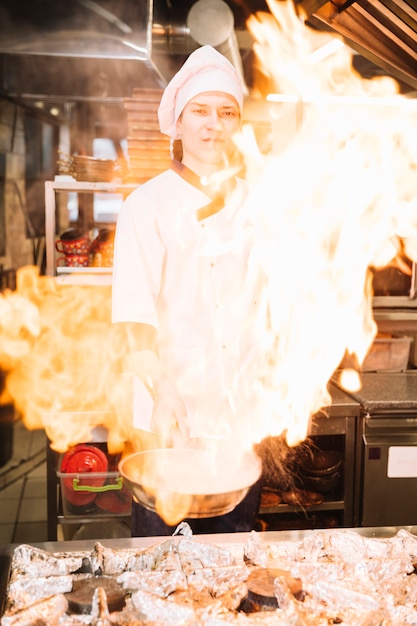 Mannelijke kok met brandende pan in de hand