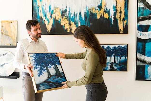 Mannelijke kunstenaar die zijn schilderij toont aan een vrouwelijke klant die geïnteresseerd is in het kopen van kunstwerken van de tentoonstelling van de kunstgalerie