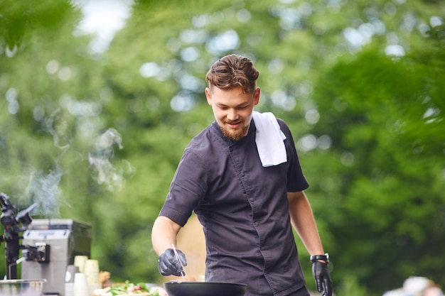 Mannelijke lachende chef-kok koken met pan buitenshuis