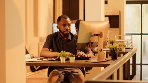 Gratis foto mannelijke manager die tijd op polshorloge controleert en aan webpresentatie werkt met online onderzoeksinformatie. analyseren van netwerkdata op de computer om een bedrijfsrapport te maken tijdens zonsondergang.