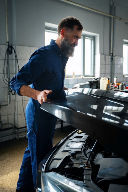 Gratis foto mannelijke monteur werkt in autoreparatiewerkplaats aan auto