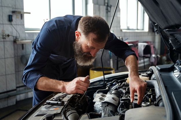 Gratis foto mannelijke monteur werkt in autoreparatiewerkplaats aan auto