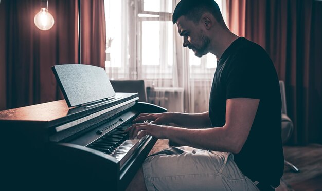 Mannelijke muzikant speelt de elektronische piano in de kamer