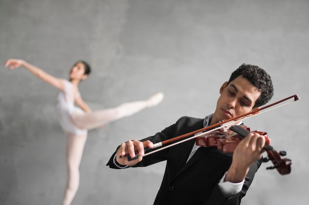 Gratis foto mannelijke muzikant speelt viool terwijl onscherpe ballerina dansen