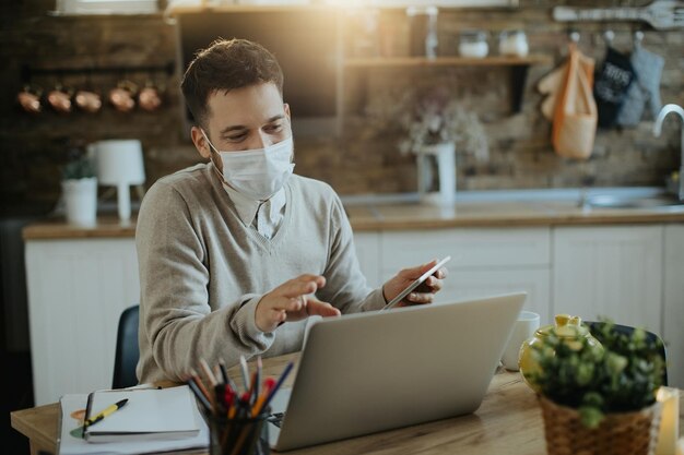 Mannelijke ondernemer met gezichtsmasker met videogesprek via laptop terwijl hij thuis werkt