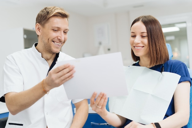 Mannelijke professionele tandarts met handschoenen en masker met papieren foto en laten zien hoe de behandeling eruit zal zien van de tanden van de patiënt