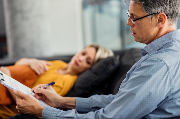 Gratis foto mannelijke psychiater die aantekeningen maakt tijdens counseling met een patiënt op zijn kantoor