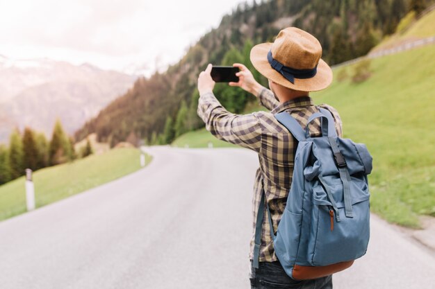 Mannelijke reiziger in trendy geruit hemd die foto maakt van verbazingwekkend landschap met bos en bergen