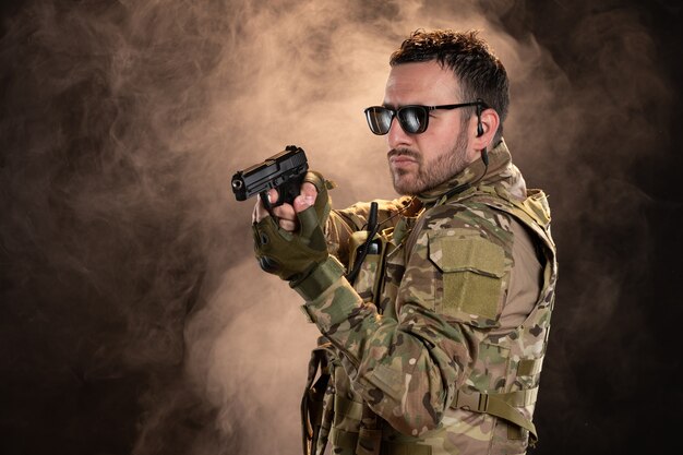 Mannelijke soldaat in camouflage die een pistool op de donkere muur richt