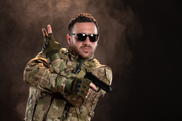 Mannelijke soldaat in camouflage die een pistool op de donkere muur richt