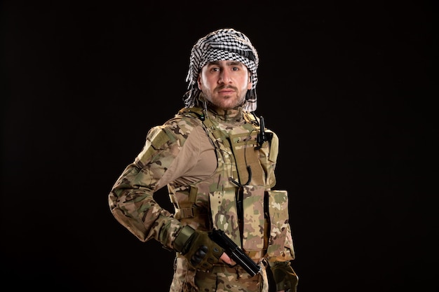 Mannelijke soldaat in camouflage gevechten met pistool op zwarte muur