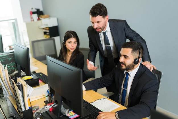 Mannelijke supervisor die een latijns-executive opleidt in een callcenter. manager die werkdingen uitlegt aan de werknemers die technische ondersteuning en klantenservice bieden