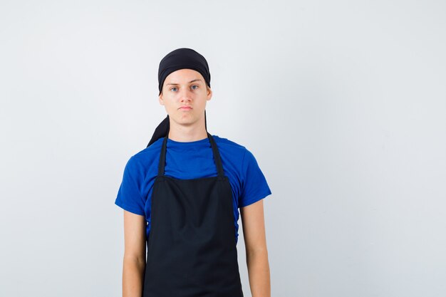 Mannelijke tienerkok poseren in t-shirt en schort en ziet er zelfverzekerd uit, vooraanzicht.