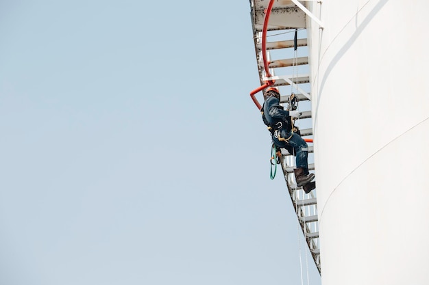 Mannelijke werknemer beneden hoogte tank schaal plaat touw ladder toegang veiligheidsinspectie van dikte opslagtank gas propaan.