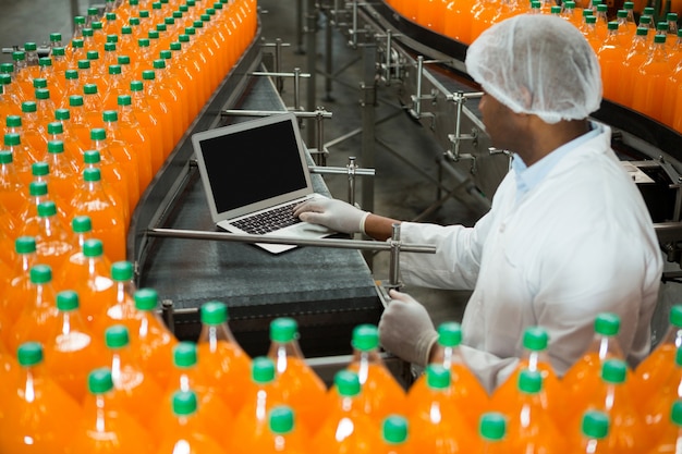 Gratis foto mannelijke werknemer met behulp van laptop te midden van de productielijn in de sapfabriek