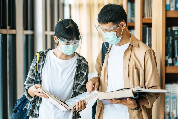 Mannen en vrouwen met maskers staan en lezen in de bibliotheek.