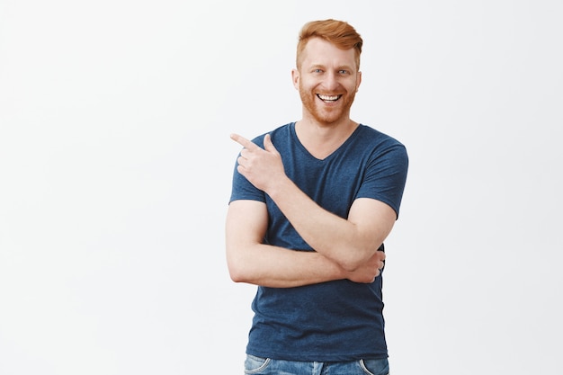 Gratis foto mannen praten in pub, bespreken recente wedstrijd. portret van knappe, zorgeloze en zelfverzekerde roodharige man met borstelharen, wijzend naar de linkerbovenhoek en vrolijk glimlachend, informeel praten en plezier hebben