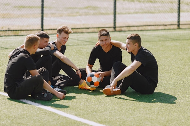 Mannen spelen voetballer in het park. Toernooi op mini-footbal. Kerel in zwarte sportpakken.