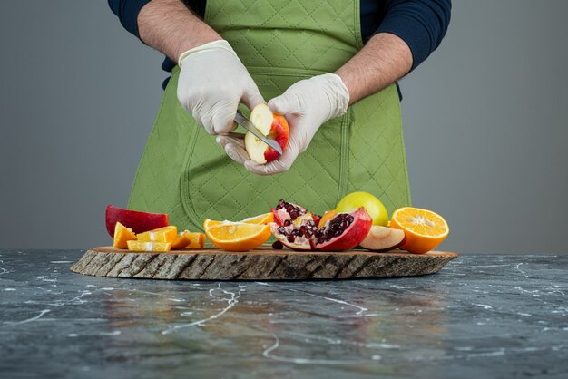 Mannenhand in handschoenen die rode appel op marmeren lijst snijden.