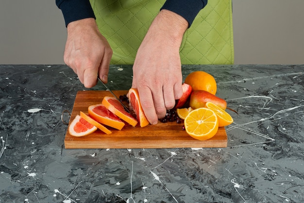 Mannenhand in handschoenen die sappige grapefruit snijden op marmeren tafel.