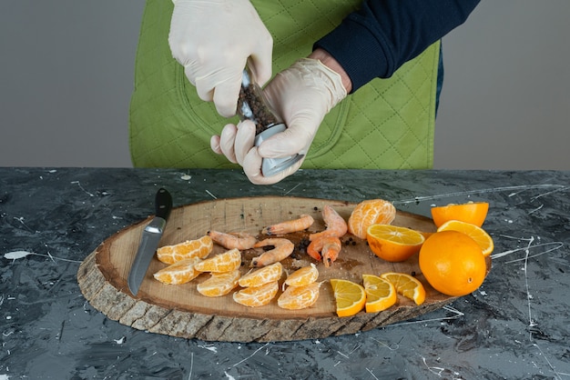 Mannenhand in handschoenen zout toevoegen aan garnalen op marmeren tafel.