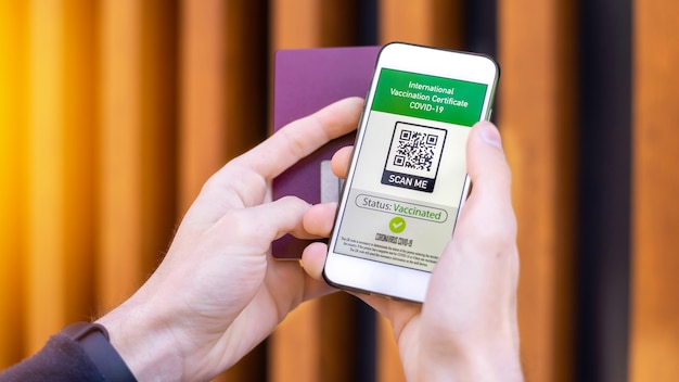 Mannenhand met paspoort en smartphone met internationaal vaccinatiecertificaat COVID-19 QR-code