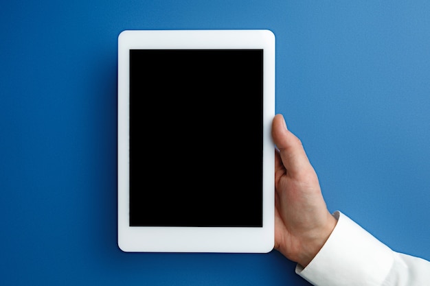 Gratis foto mannenhand met tablet met leeg scherm op blauw