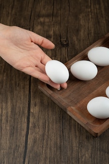 Mannenhand nemen rauw biologisch ei uit een houten bord.