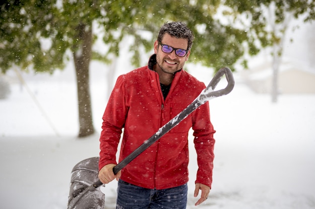 Mannetje dat een sneeuwschop houdt en een rood jasje draagt terwijl het glimlachen