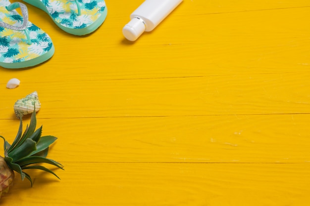 Mariene reizen, zonnebrandcrèmes, slippers en ananas op een gele houten vloer.