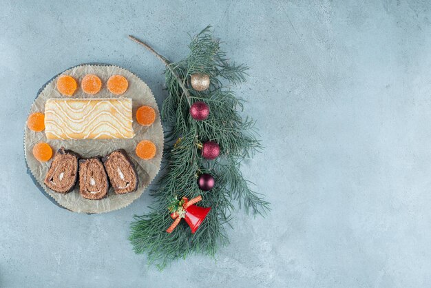 Marmelades en een cakerol met plakjes op een schaal met een versierde dennentak op marmer.