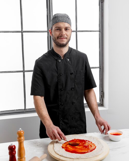 Medio geschoten mens die tomatensaus op pizzadeeg verspreidt