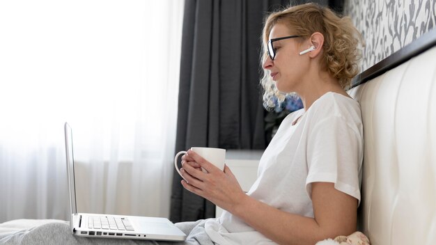 Medio geschotene blonde vrouw die aan laptop werkt en koffie drinkt