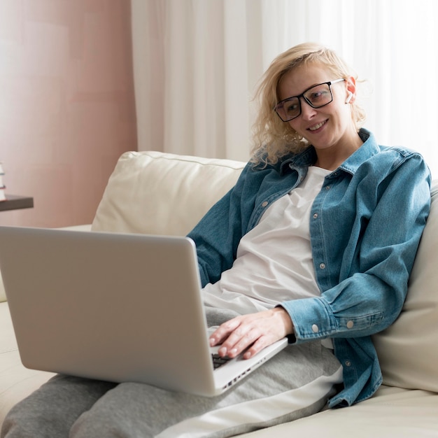 Medio geschotene blonde vrouwenzitting op laag en het werken aan laptop