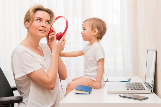 Medio geschotene de hoofdtelefoons en baby van de moederholding op bureau