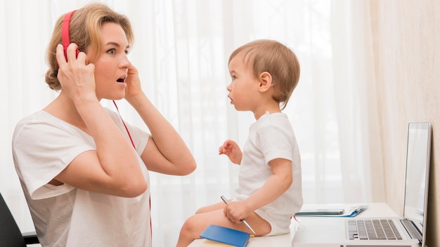 Gratis foto medio geschotene moeder met hoofdtelefoons en baby op bureau