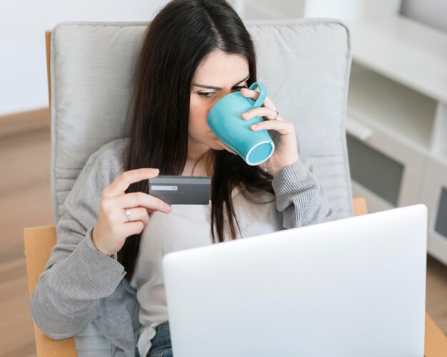 Medio geschotene vrouwenzitting op stoel met laptop en het drinken van koffie