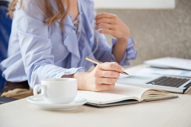 Medio sectie die van anonieme vrouw nota's maken die bij bureau zitten