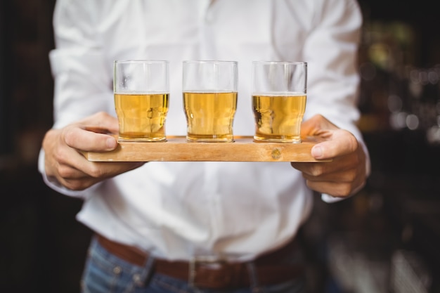 Gratis foto medio sectie van het dienblad van de barmanholding van whisky geschotene glazen bij barteller